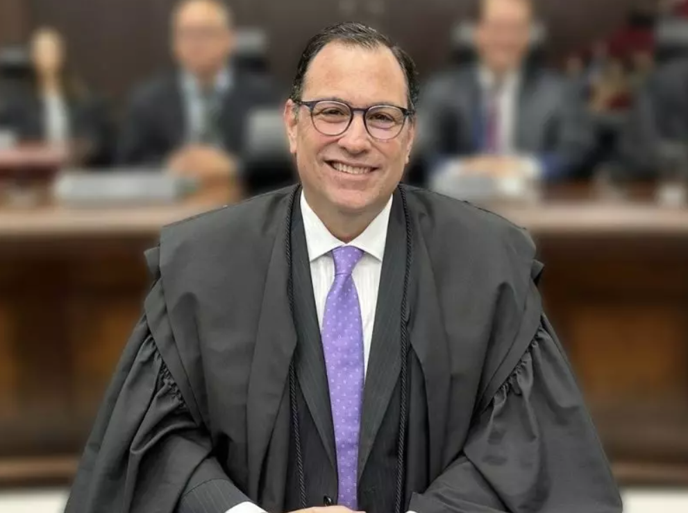 desembargador com vestimenta jurídica, em pose sorrindo. 