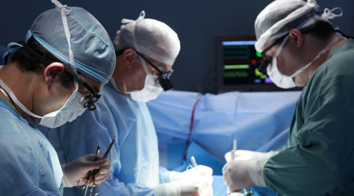 Equipe médica em centro cirúrgico realizando procedimento hospitalar com equipamentos e vestimentas adequadas.