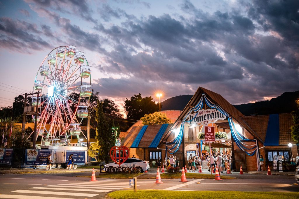 Público circula pela entrada do Parque Municipal de Eventos durante a Festa Pomerana, em Pomerode, com decoração típica alemã e iluminação noturna