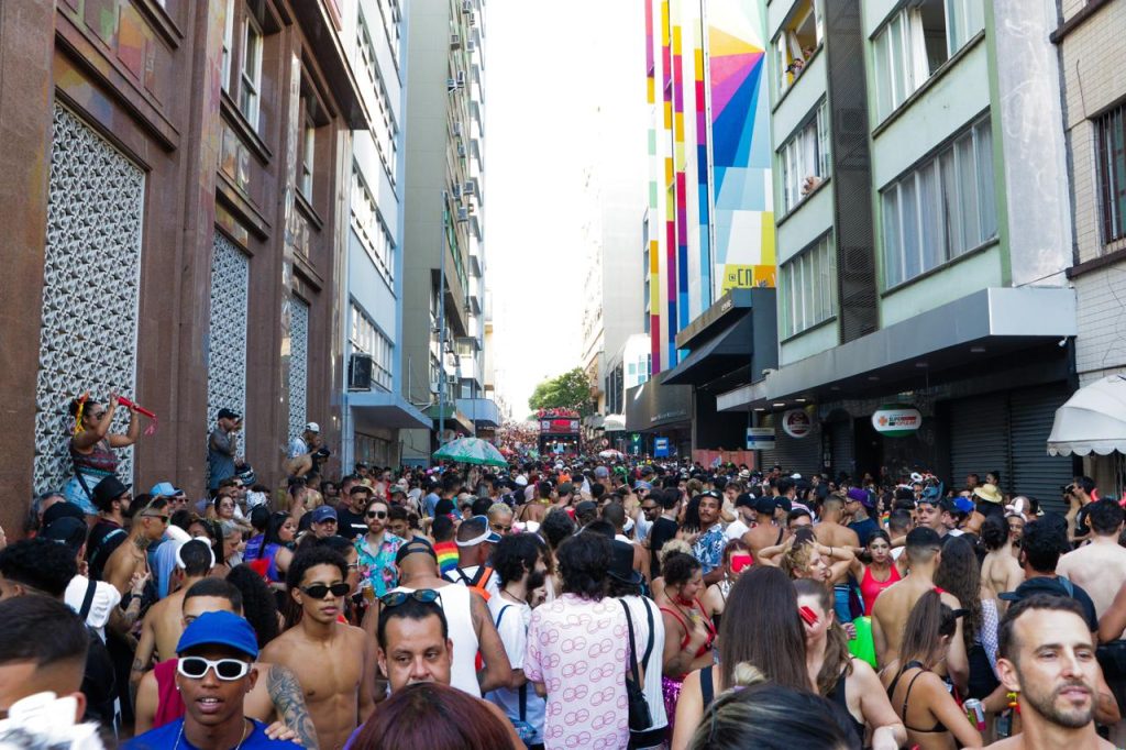 Multidão de foliões ocupa rua do centro de Florianópolis durante desfile de bloco de Carnaval, com prédios ao redor e pessoas reunidas em clima festivo.