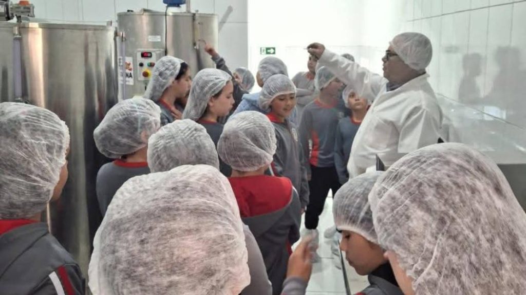 Estudantes participam de atividade educativa do Projeto Sanitarista Júnior durante visita técnica a agroindústria, acompanhados por profissional da área sanitária.